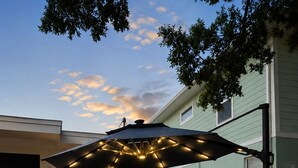 An outdoor patio with two wicker chairs, a small table, and a large umbrella with lights. - The Lincoln Luxe Studio• Private Retreat • Midtown • Downtown • Stadium  (Tampa)