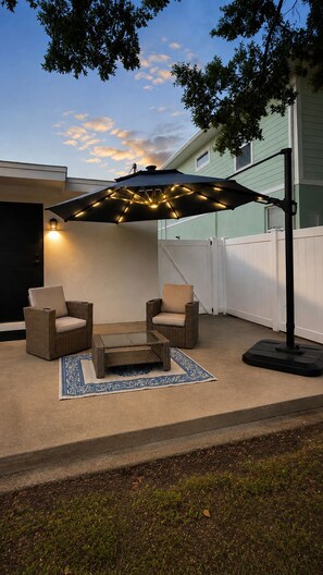 An outdoor patio with two wicker chairs, a small table, and a large umbrella with lights. - The Lincoln Luxe Studio• Private Retreat • Midtown • Downtown • Stadium  (Tampa)