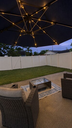 An outdoor patio area with a large umbrella, wicker furniture, and a glass-top coffee table. - The Lincoln Luxe Studio• Private Retreat • Midtown • Downtown • Stadium  (Tampa)