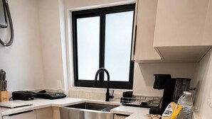 A modern kitchen with a stainless steel sink, a window, a countertop with a coffee maker, and a stool. - The Lincoln Luxe Studio• Private Retreat • Midtown • Downtown • Stadium  (Tampa)