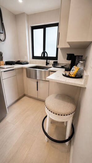 A modern kitchen with a stainless steel sink, a window, a countertop with a coffee maker, and a stool. - The Lincoln Luxe Studio• Private Retreat • Midtown • Downtown • Stadium  (Tampa)