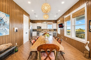 A spacious kitchen with wooden cabinets, a large island, and a dining area with a long table and chairs. - Beachfront + Canal: 4BR/4BA w/ Ocean Views & Fireplace (Port Bolivar)