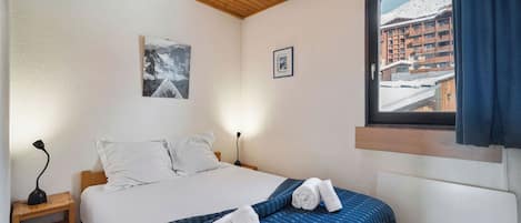 A bedroom with a bed, a nightstand, a lamp, a window with a view of a snowy landscape, and a framed picture on the wall.