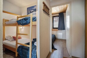 A room with bunk beds, a window with curtains, and a view of buildings outside. - Résidence les Eterlous (Les Belleville)