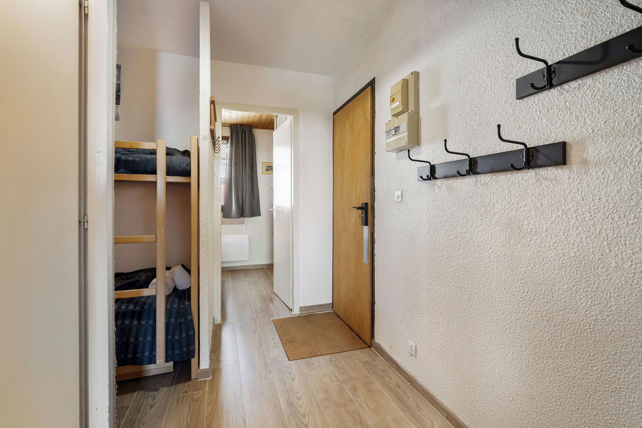 A narrow hallway with a wooden door, a coat rack, and a bunk bed.