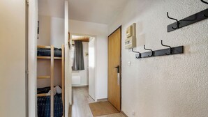A narrow hallway with a wooden door, a coat rack, and a bunk bed. - Résidence les Eterlous (Les Belleville)