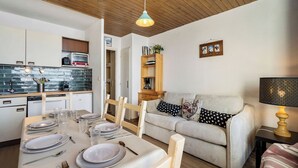 A modern kitchen with a dining area set for a meal, a sofa, and a lamp. - Résidence les Eterlous (Les Belleville)