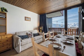 Een knus woongedeelte met een bank, een eettafel gedekt voor twee personen, en uitzicht op een skilift.