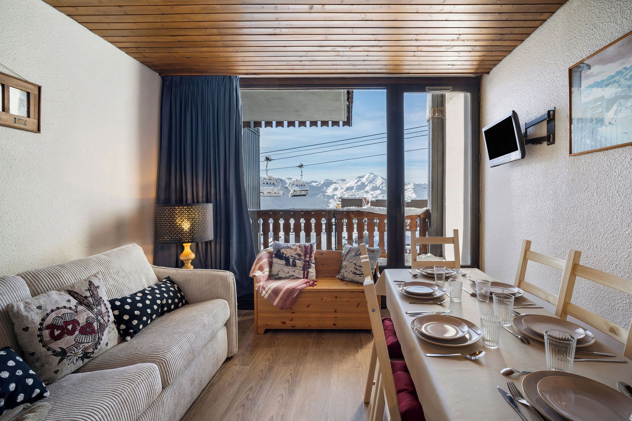 A cozy room with a sofa, a dining table set for two, and a view of snow-capped mountains through a large window.