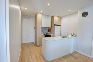 A modern kitchen with a central island, built-in appliances, and a wooden floor. - The Aristocrat | Mid Century Luxe Dual Suite + Gym (Dickson)