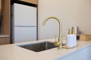 Eine Küchenspüle mit einem goldenen Wasserhahn, einem weißen Seifenspender und einer Holzseifenschale.