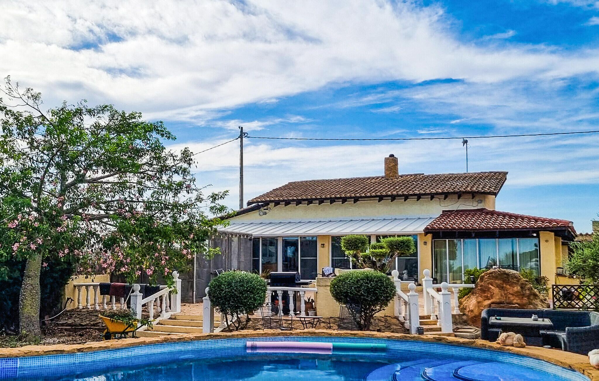 A house with a swimming pool, a covered patio, and a garden with a white fence.