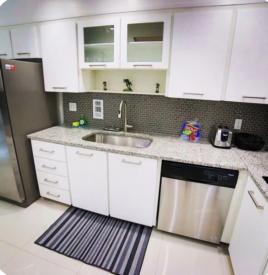A kitchen with white cabinets, a stainless steel refrigerator, a dishwasher, and a tiled backsplash.