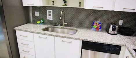 A kitchen with white cabinets, a stainless steel refrigerator, a dishwasher, and a tiled backsplash.