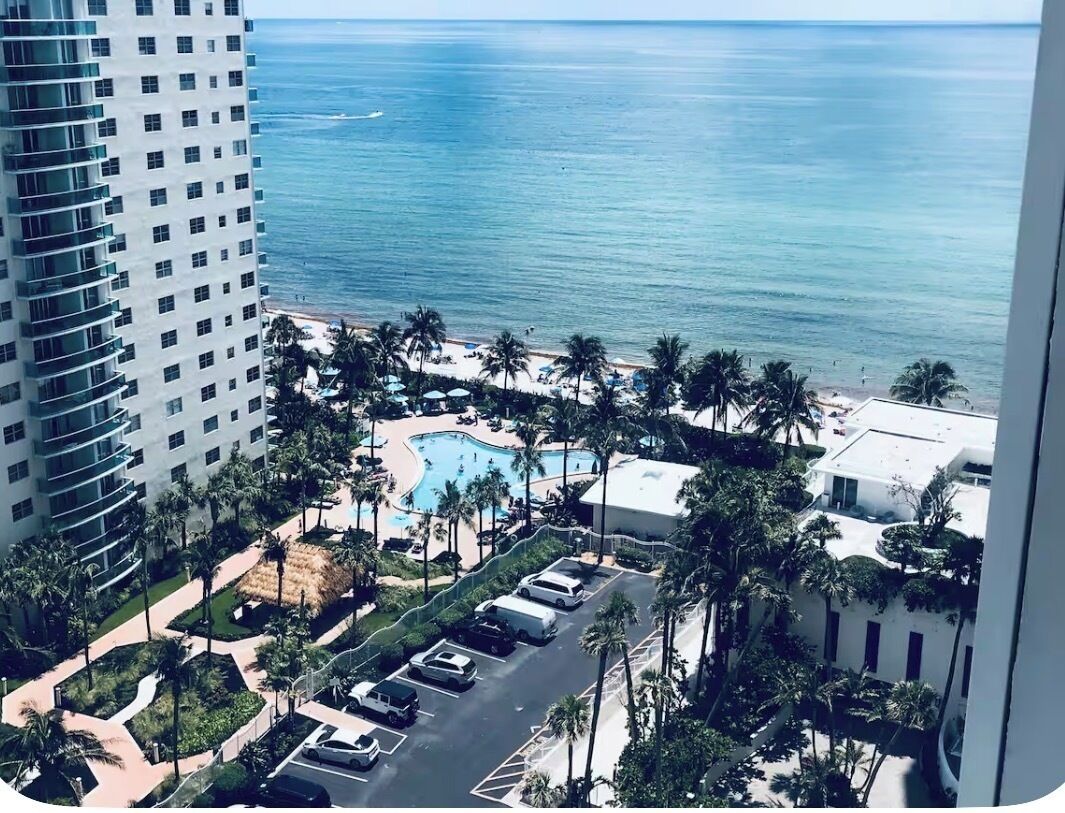 A high-rise hotel with a view of the ocean and a pool area with palm trees.