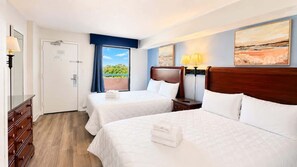 Ein Hotelzimmer mit zwei Betten, einer Holzkommode, einer Tür und Blick auf Grünflächen.