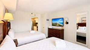 Une chambre d’hôtel avec deux lits, une commode, un téléviseur et vue sur la plage.