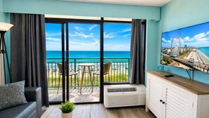 A room with a balcony, a TV, a sofa, and a small table. - Wake Up to Ocean Views | 6th Floor 1BR + Pool (Myrtle Beach)