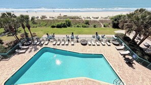 Ein Pool mit Blick auf den Strand, umgeben von Liegestühlen und Palmen.