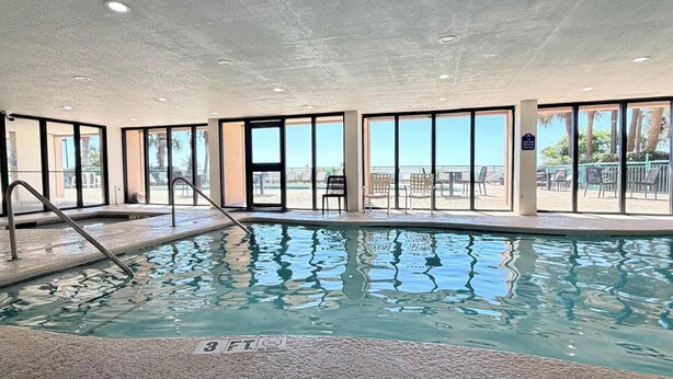 An indoor swimming pool with clear glass walls, a diving board, and a view of the beach. - Wake Up to Ocean Views | 6th Floor 1BR + Pool (Myrtle Beach)