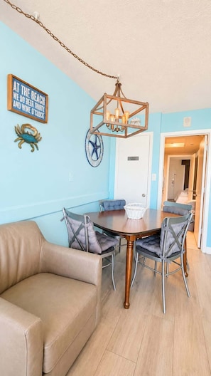 Un coin repas avec une table ronde, des chaises, un luminaire suspendu et un mur orné d’une enseigne et d’un décor représentant un crabe.