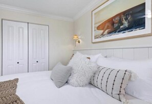 Een slaapkamer met een bed, witte muren, een ingelijst beeld en een witte deur.