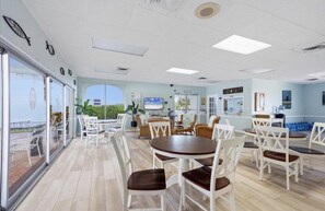 A spacious indoor area with multiple seating arrangements, including round tables and chairs, and a large window providing a view of the outdoors. - Condo#215 Siesta Key Condominium (Sarasota)