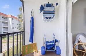Ein Balkon mit Blick auf ein Gebäude, ein blauer Stuhl, ein Kinderwagen und ein an der Wand befestigtes Regal mit einem Handtuch.