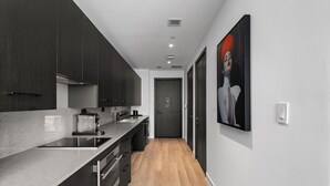 A modern kitchen with dark cabinets, a marble countertop, and a wooden floor. - Executive Suite At The E11EVEN Residences (Miami)