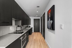 A modern kitchen with dark cabinets, a marble countertop, and a wooden floor. - Executive Suite At The E11EVEN Residences (Miami)