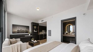A modern hotel room with a large bed, a sofa, a desk, a kitchen area, and a bathroom with a mirror. - Executive Suite At The E11EVEN Residences (Miami)