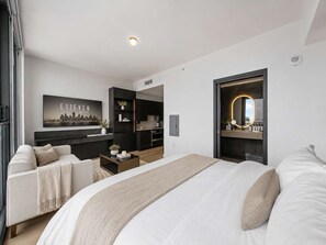 A modern hotel room with a large bed, a sofa, a desk, a kitchen area, and a bathroom with a mirror. - Executive Suite At The E11EVEN Residences (Miami)