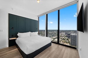 Un dormitorio moderno con una cama grande, televisión y vistas a la ciudad a través de amplios ventanales.