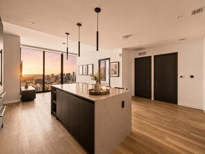 A modern kitchen with a large island, pendant lighting, and a view of the city at sunset. - 48th Floor E11EVEN 2BR Bay Views ELITE Amenities (Miami)