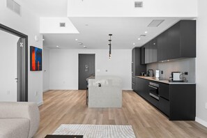 A modern kitchen with dark cabinetry, a central island, and a dining area with a light-colored sofa. - E11EVEN 48th Floor | Bay Views & Rooftop Pool (Miami)