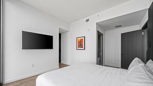 Une chambre à coucher moderne avec un grand lit, un téléviseur à écran plat fixé au mur et une œuvre d’art encadrée accrochée au mur.