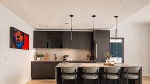 Une cuisine moderne dotée d’un îlot central, de tabourets de bar et de luminaires suspendus.