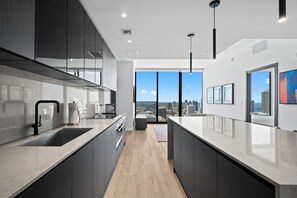 A modern kitchen with a large island, dark cabinetry, and a city view through large windows. - E11EVEN 48th Floor Bay Views & Rooftop Pool (Miami)