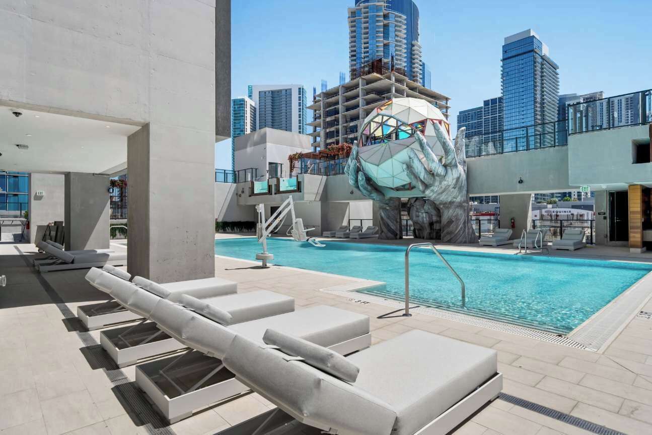 A rooftop pool with lounge chairs, a unique sculpture, and a city skyline in the background.