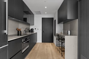 A modern kitchen with dark cabinetry, stainless steel appliances, and a wooden floor. - E11EVEN Skyline Suite 29th Floor w/ Rooftop Pool (Miami)