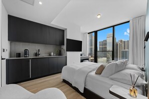 A modern bedroom with a large bed, a built-in kitchen with dark cabinets, a flat-screen TV, and a city view through large windows. - E11EVEN Skyline Suite 29th Floor w/ Rooftop Pool (Miami)