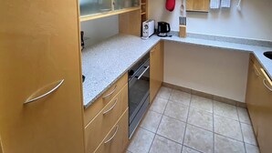 A compact kitchen with wooden cabinets, a countertop, a skylight, and a small window. - Luxury Moments Begin, Wallis 1077 (Wallis)