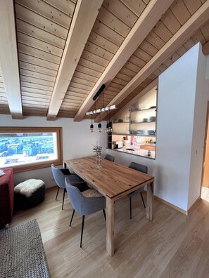 Une cuisine moderne avec des poutres en bois, une table à manger avec des chaises et une vue sur la ville par une grande fenêtre.