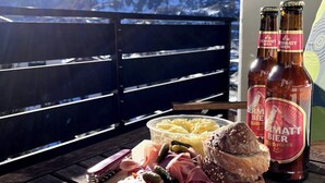A table with a cheese platter, meats, and nuts, with bottles of Zermatt Bier beer and a view of mountains. - Luxury Moments Begin, Wallis 1077 (Wallis)
