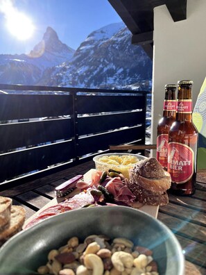 Ein Tisch mit einer Käseplatte, Fleisch und Nüssen, dazu Flaschen Zermatt Bier und ein Blick auf die Berge.