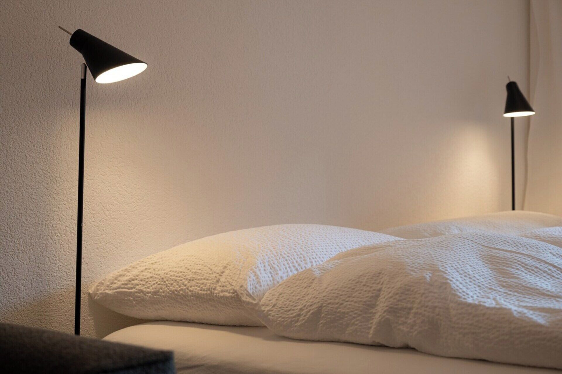 A bed with white bedding and two black floor lamps on either side.