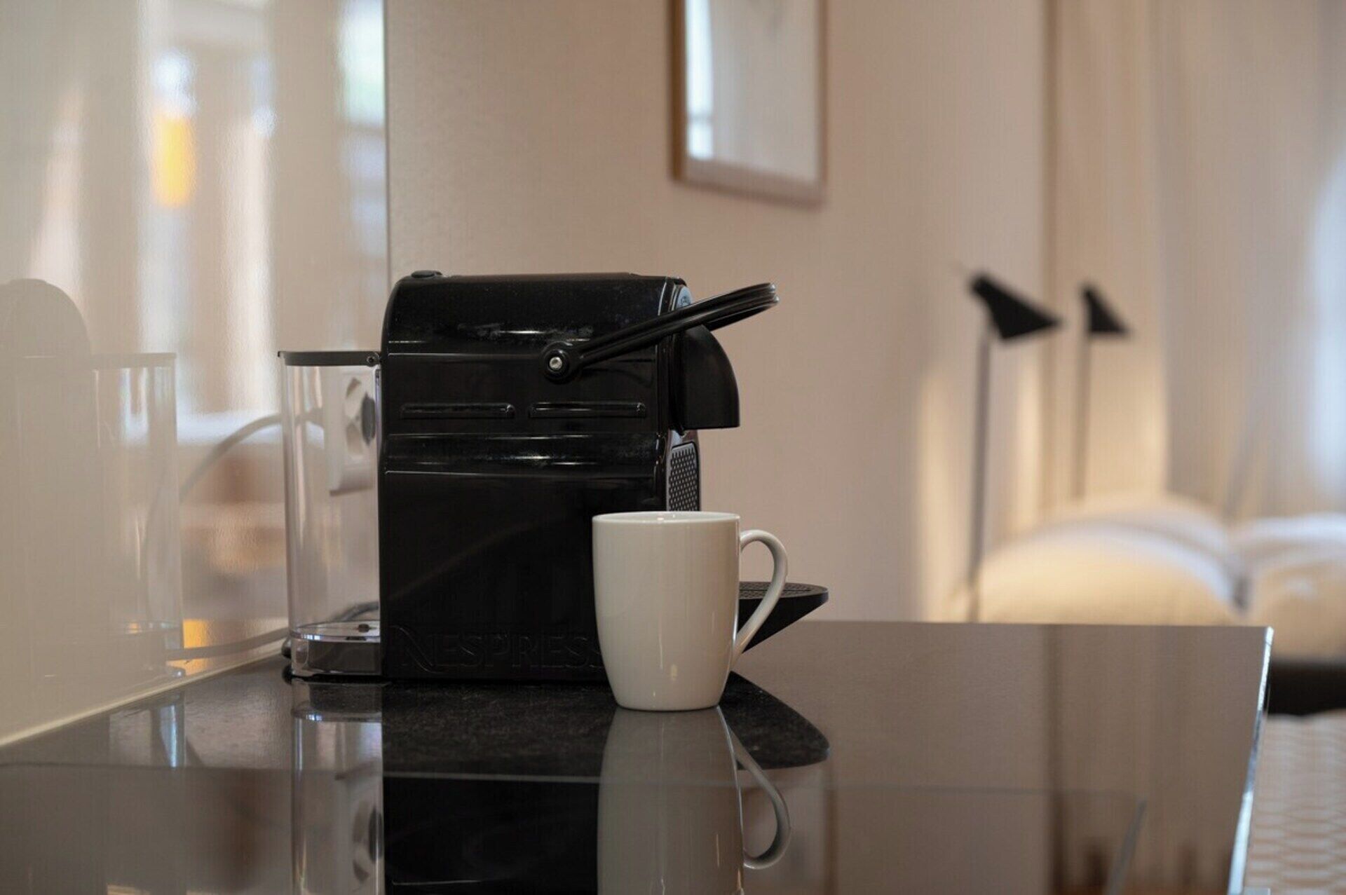 En Nespresso-kaffemaskin står på ett bord, och bredvid den finns en vit mugg.