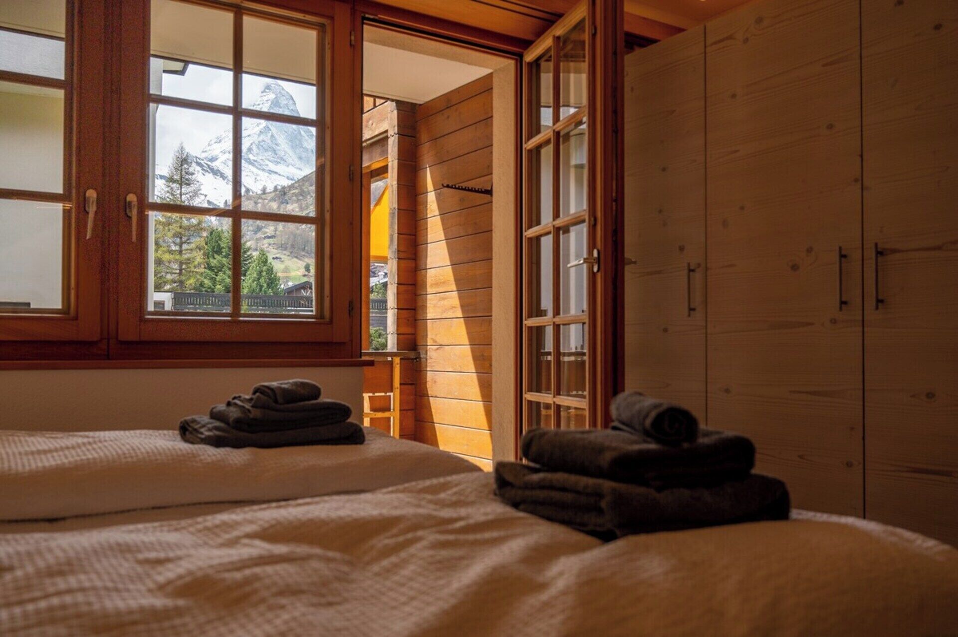 A bedroom with two beds, a wooden wardrobe, and a window with a mountain view.