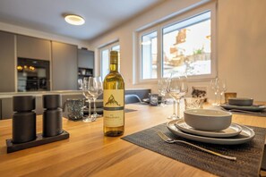 A dining table set with a bottle of wine, glasses, and plates in a modern kitchen with large windows. - Breathtaking Luxury Stay, Wallis 1079 (Wallis)