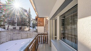 A balcony with a wooden railing, a view of snow-covered ground, and a building with a large window. - Breathtaking Luxury Stay, Wallis 1079 (Wallis)